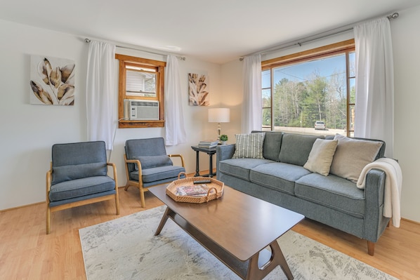 A living room with a grey sofa, two armchairs, a wooden coffee table, and a large window with curtains. - Hike, Ski & Ice Fish! Cozy Bungalow in Cedar (Cedar)