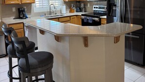 A modern kitchen with wooden cabinets, a stainless steel refrigerator, and a central island with bar stools. - Havasu Pool Home with A/C Boat Garage + Toy Parking (Lake Havasu City)