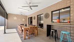 A spacious patio area with a wooden table and chairs, a black bar stool, and a ceiling fan. - Calm Waters, Moonta Bay (Moonta Bay)