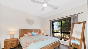 A bedroom with a wooden bed, two bedside tables, a ceiling fan, a large window with curtains, and a framed artwork on the wall. - Calm Waters, Moonta Bay (Moonta Bay)