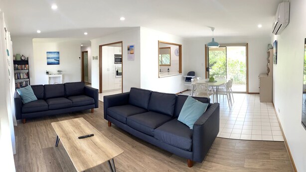 A modern living room with two dark sofas, a wooden coffee table, and a dining area with a white table and chairs. - Just Beachy, Port Victoria (Port Victoria)