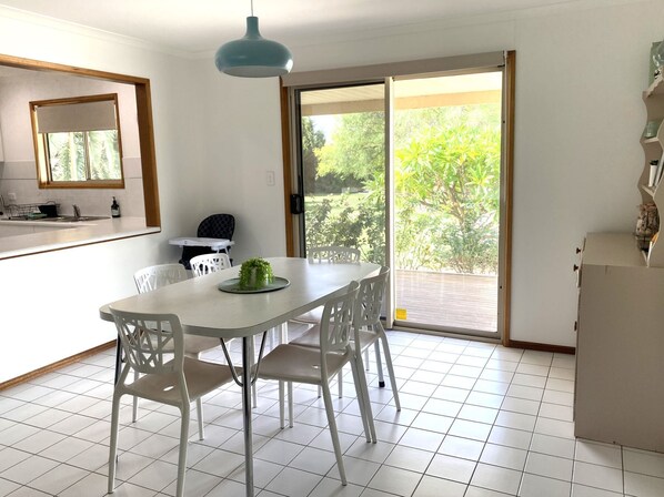 A dining area with a white table and chairs, a blue pendant light, a small indoor plant, and a sliding glass door leading to an outdoor patio.