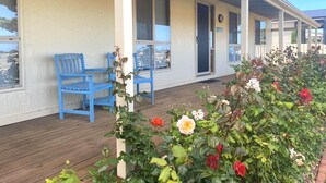 A covered porch with blue chairs and a flower bed with various flowers. - Just Beachy, Port Victoria (Port Victoria)