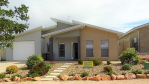Une maison moderne à deux étages, dotée d’un porche couvert, d’une allée et d’un jardin paysager à l’avant, agrémenté de rochers et d’arbustes.