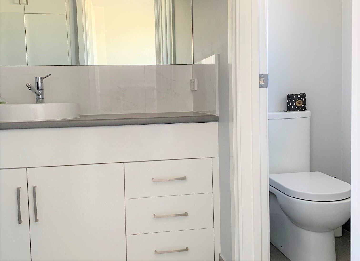 A modern bathroom with a white sink, mirror, and toilet.