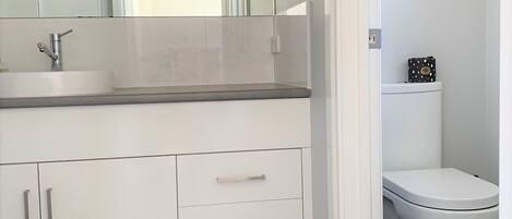 A modern bathroom with a white sink, mirror, and toilet.