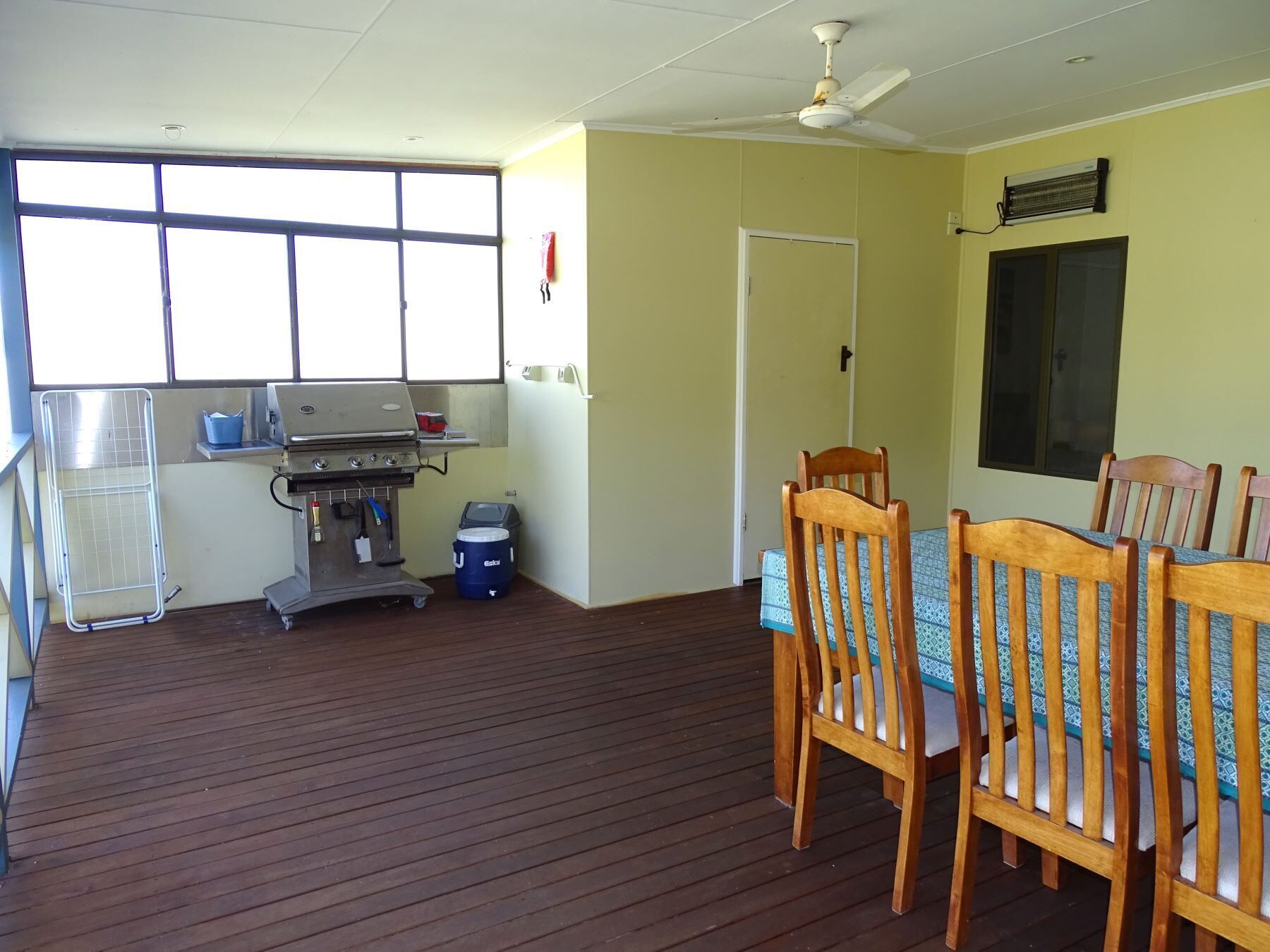 A room with a wooden floor, a table with chairs, a ceiling fan, a grill, and a window with blinds.