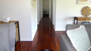 A hallway with wooden flooring, a gray sofa, a wooden side table, and a white wall with a painting. - Ardy House, Ardrossan (Ardrossan)
