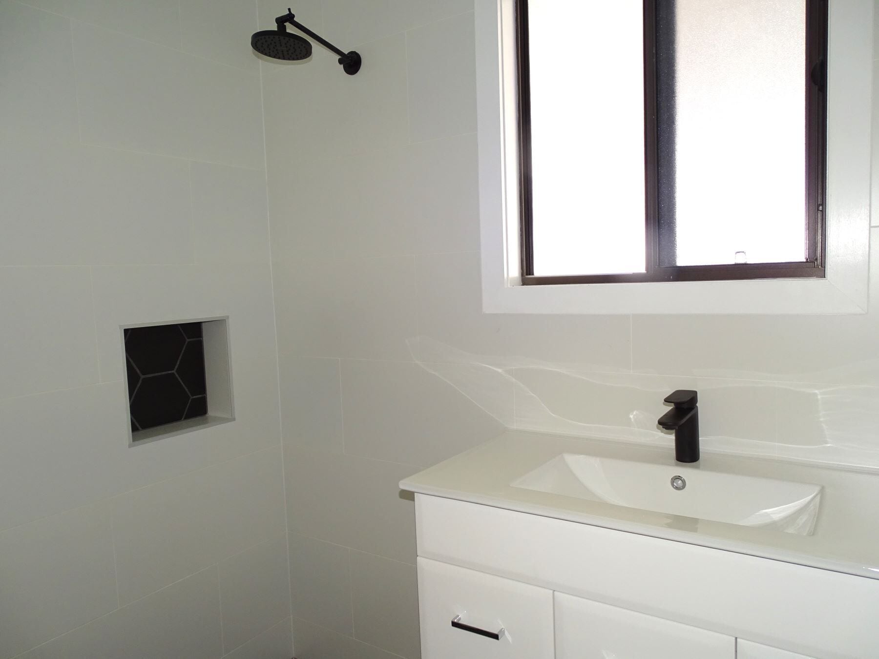 A bathroom with a white sink, a mirror, and a showerhead.