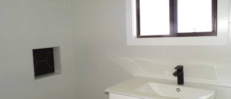 A bathroom with a white sink, a mirror, and a showerhead.
