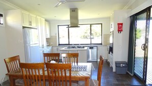 A modern kitchen with white cabinets, a dining table with chairs, a stove, and a dishwasher. - Ardy House, Ardrossan (Ardrossan)