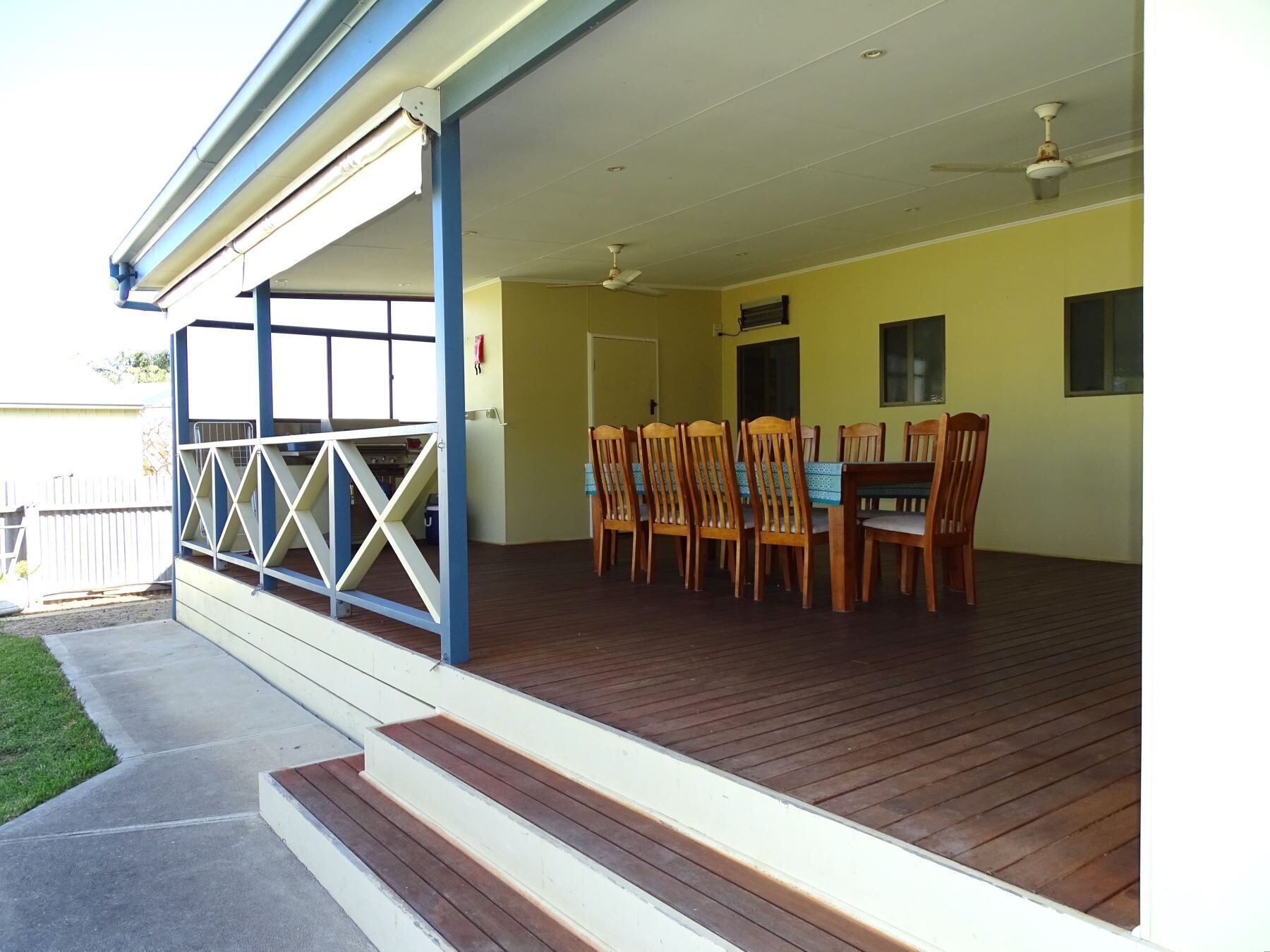 Un espace extérieur abrité, aménagé pour les repas, avec une terrasse en bois, une table et des chaises, ainsi qu’un ventilateur de plafond.
