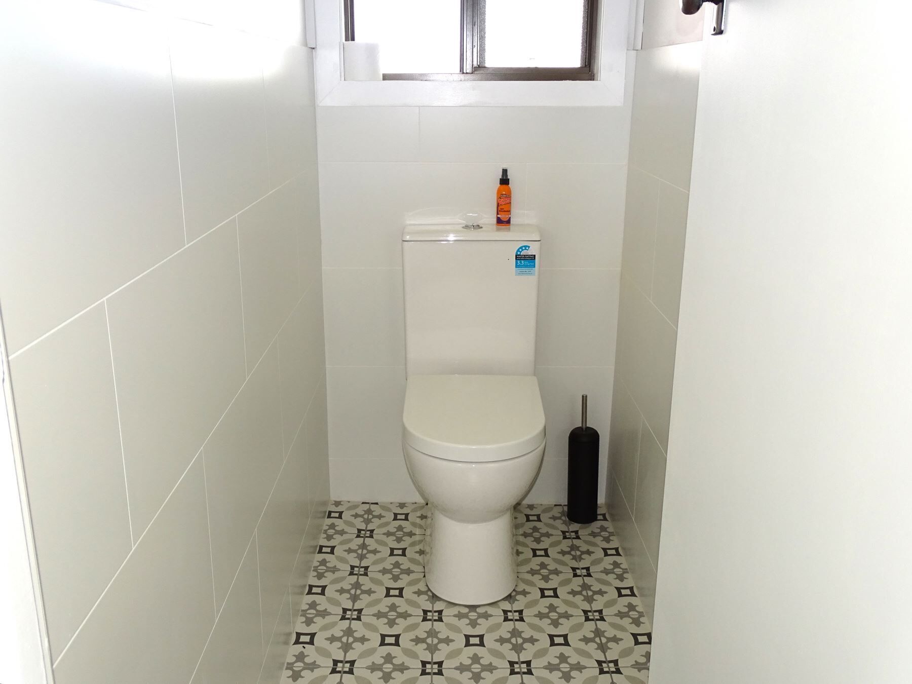A small bathroom with a toilet, a toilet brush, and a bottle of cleaning product.