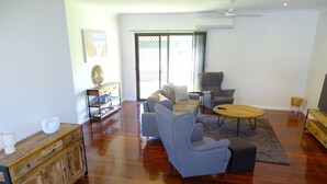 A spacious living room with a wooden floor, a grey sofa set, a coffee table, and a television on a wooden stand. - Ardy House, Ardrossan (Ardrossan)