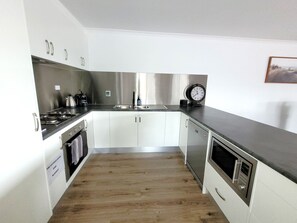 Una cocina moderna con electrodomésticos de acero inoxidable, armarios blancos y piso de madera.
