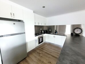 A modern kitchen with white cabinets, stainless steel appliances, and a wooden floor.