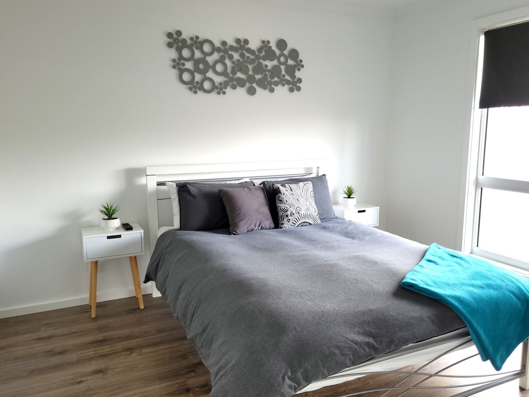 A modern bedroom with a grey bed, white headboard, and a decorative wall piece.
