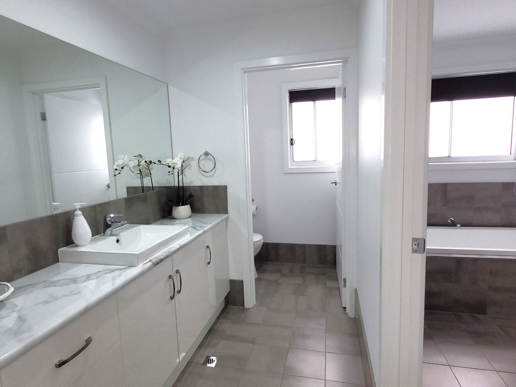 A modern bathroom with a large mirror, a sink, and a toilet.