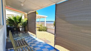 Een overdekt terras met een zwart-wit betegelde vloer, een houten bank en uitzicht op het strand en de zee.