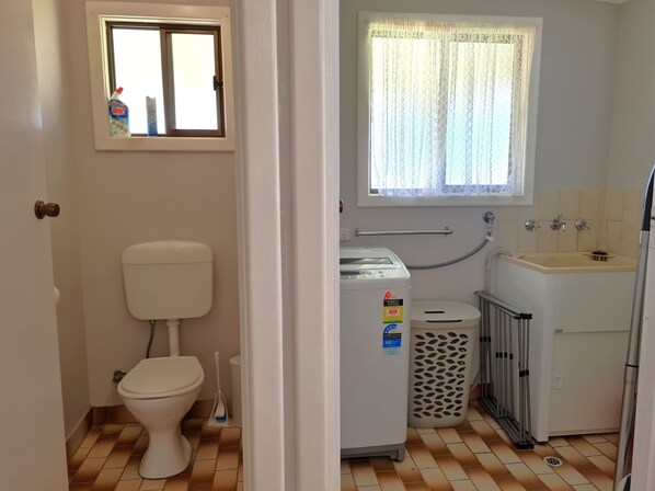 A small, compact bathroom with a toilet, a washing machine, a sink, and a window with curtains. - Reel Relaxation, Fisherman Bay (Fisherman Bay)