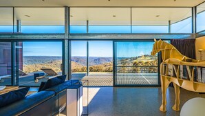 A modern living room with a large glass wall offering a scenic view of hills and trees. - Mountain Top Bilpin, Studio 1 Isyd (Bilpin)