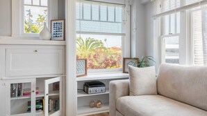 A cozy living room with a large window, a bookshelf, a sofa, and a small table with decorative items. - Cliff View by Avantstay Hot Tub + Fire Pit 1 Block From Downtown La Jolla (La Jolla)