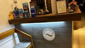 Ein Empfangsbereich mit einer hölzernen Sitzbank, einem an der Wand befestigten Logo und verschiedenen Werbeartikeln auf einem Regal.