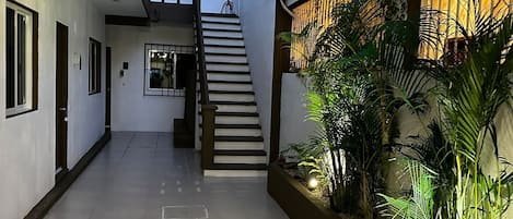 A clean, modern interior with a staircase leading to an upper floor, a hallway with doors, and a planter with tropical plants.