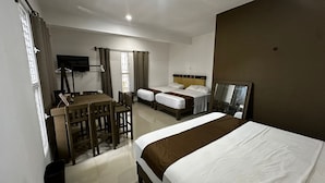 Ein Hotelzimmer mit einem großen Bett, einem Schreibtisch mit Stuhl, einem Fernseher und einem Fenster mit Vorhängen.