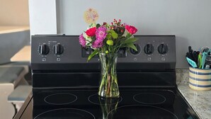 Una cocina con un microondas Frigidaire negro sobre una estufa negra, un florero con flores en la estufa y un organizador de utensilios en la encimera.