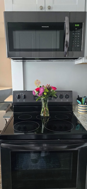 A kitchen with a black Frigidaire microwave above a black stove, a vase with flowers on the stove, and a utensil holder on the counter.