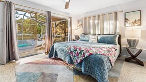 Un dormitorio con una cama grande, un ventilador de techo, una puerta de vidrio que da a una piscina y vistas al exterior.