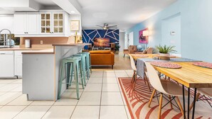 Una cocina moderna con armarios blancos, una isla central con taburetes y un área de comedor con mesa y sillas de madera.