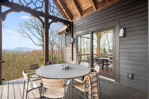 A wooden deck with a round table and chairs, overlooking a mountainous landscape. - Windy Hill Lodge, A LUXURIOUS ESTATE (Sapphire)