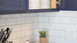 Une cuisine avec des meubles de couleur sombre, des carreaux blancs, un bloc à couteaux, un vase blanc, une petite plante et un saladier en bois posé sur le plan de travail.