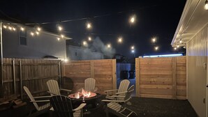 Une terrasse extérieure avec des fauteuils Adirondack, un foyer et des guirlandes lumineuses.