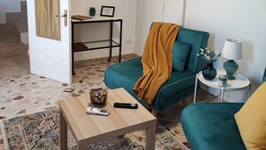 A living room with a teal sofa, a wooden coffee table, a small side table with a lamp, and a colorful abstract painting on the wall. - Vacation home in the heart of Petralia Soprana with Breakfast (Petralia Soprana)