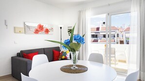 Un salón moderno con una mesa redonda blanca, un sofá gris y cojines rojos. Un jarrón con flores azules está sobre la mesa.