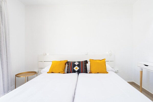 A neatly made bed with white bedding and two yellow pillows, a white bedside table, and a white nightstand. - Home2Book Sunny Poolside Apt in Las Floritas (Playa de la Américas)