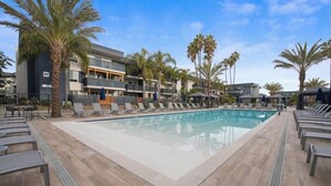 A pool area with lounge chairs, palm trees, and a modern building with balconies. - Charming studio in Newport Beach, fitness gym, pools and more! (Newport Beach)
