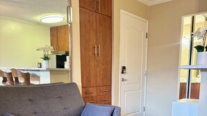 A living room with a grey sofa, wooden cabinets, and a white door. - Charming studio in Newport Beach, fitness gym, pools and more! (Newport Beach)