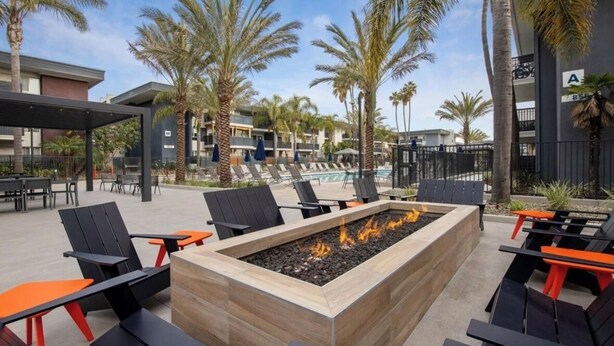 An outdoor seating area with a fire pit, lounge chairs, and a pool in the background. - Charming studio in Newport Beach, fitness gym, pools and more! (Newport Beach)