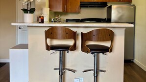 A kitchen with wooden cabinets, a stainless steel refrigerator, and two bar stools. - Charming studio in Newport Beach, fitness gym, pools and more! (Newport Beach)