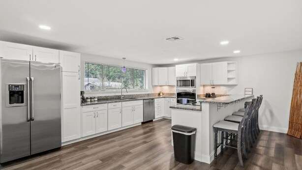 A modern kitchen with white cabinets, stainless steel appliances, a large window, and a bar area.