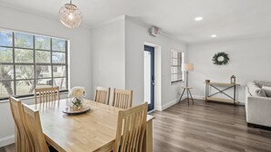 A modern dining area with a wooden table and chairs, a pendant light, and a view through large windows.