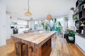 A modern kitchen with white cabinets, a wooden dining table, and a hanging pendant light.
