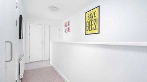 A hallway with white walls, a 'SAVE THE BEES!' poster, and a door at the end.