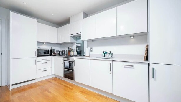 A modern kitchen with white cabinets, a built-in oven, and a wooden floor.
