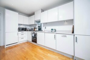 A modern kitchen with white cabinets, a built-in oven, and a wooden floor.