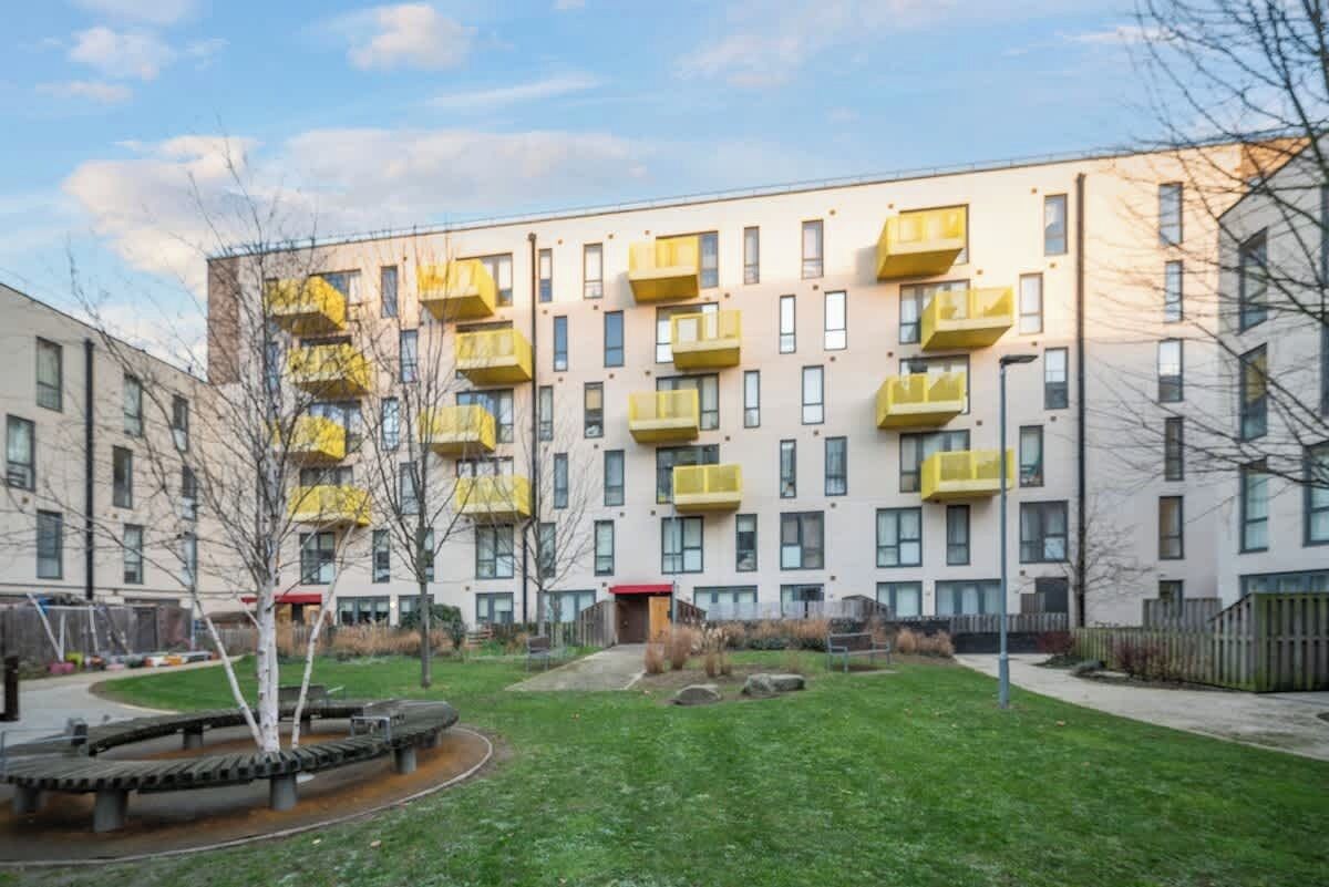 Een meerlaags woongebouw met balkons, een gazon en een speeltuin.